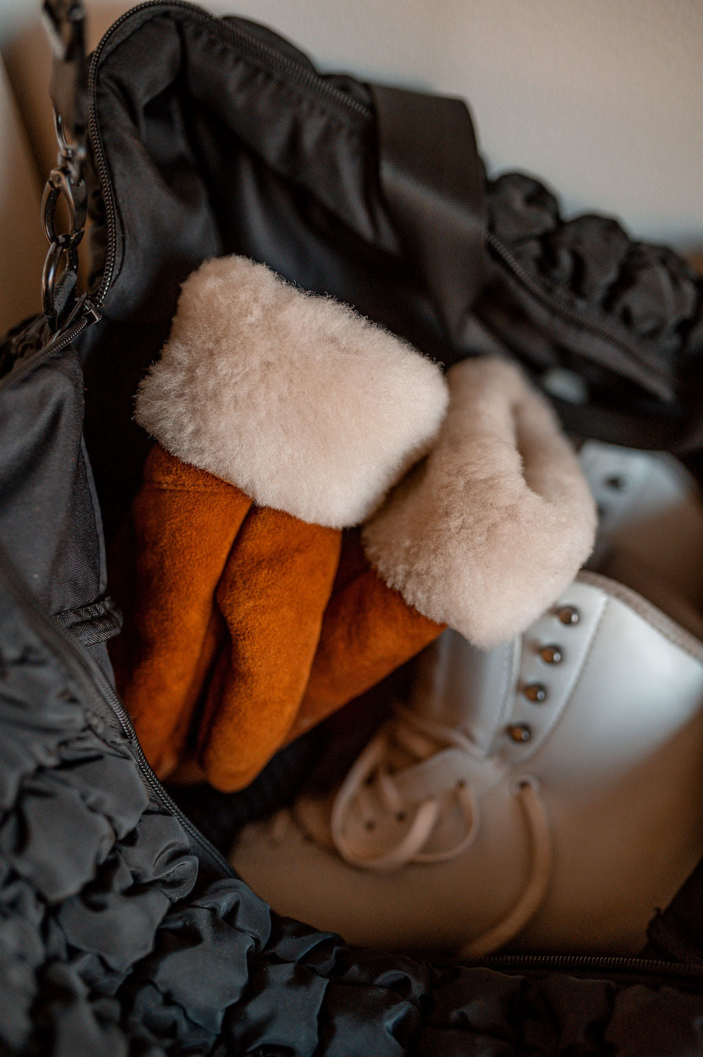 A pair of East Perry’s The Haven Sheepskin Mitten in Amber and white ice skates rest inside an open black bag.