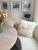 Living room with a beige sofa, round wooden table, and double sided ivory sheepskin pillowcase