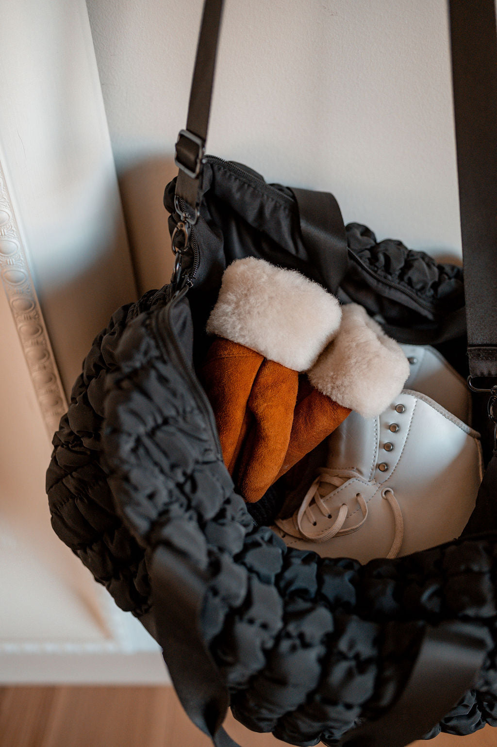 A black quilted bag holds a pair of East Perry’s The Haven Sheepskin Mittens in Amber and a pair of white ice skates.