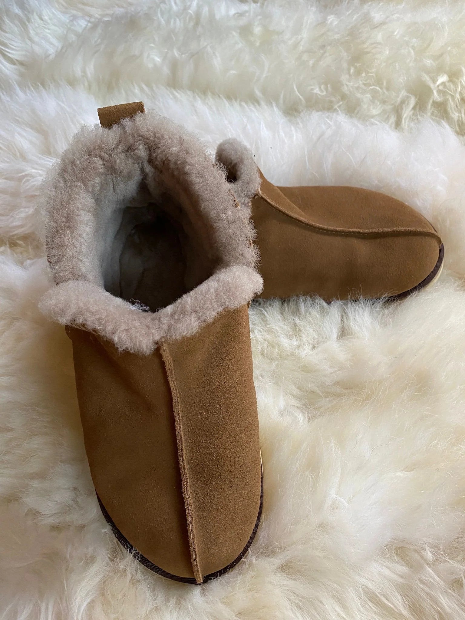 Tan slipper with fur trim on a fluffy white surface