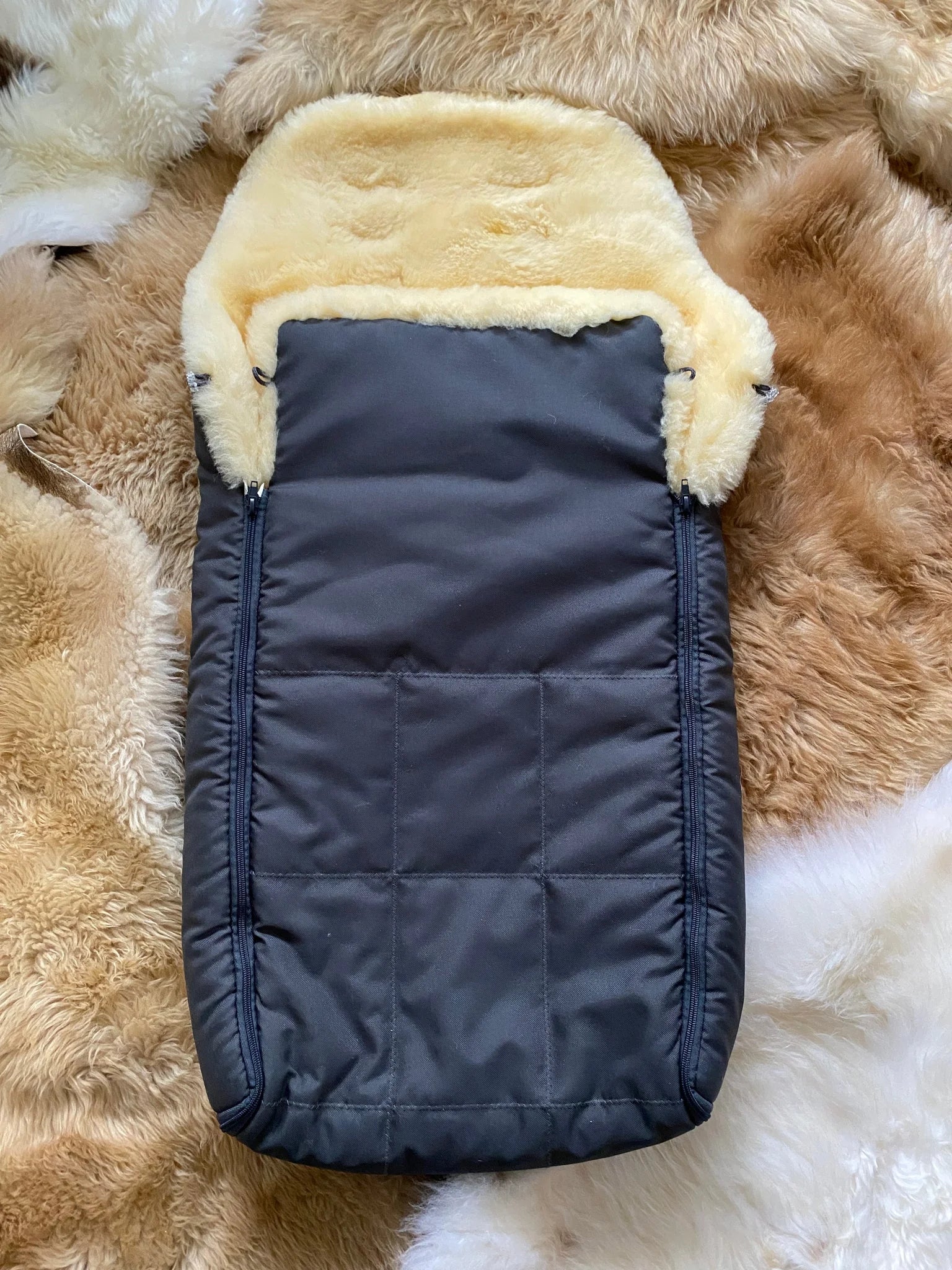 baby and toddler sleeping bag with cream sheepskin lining placed on a fluffy rug