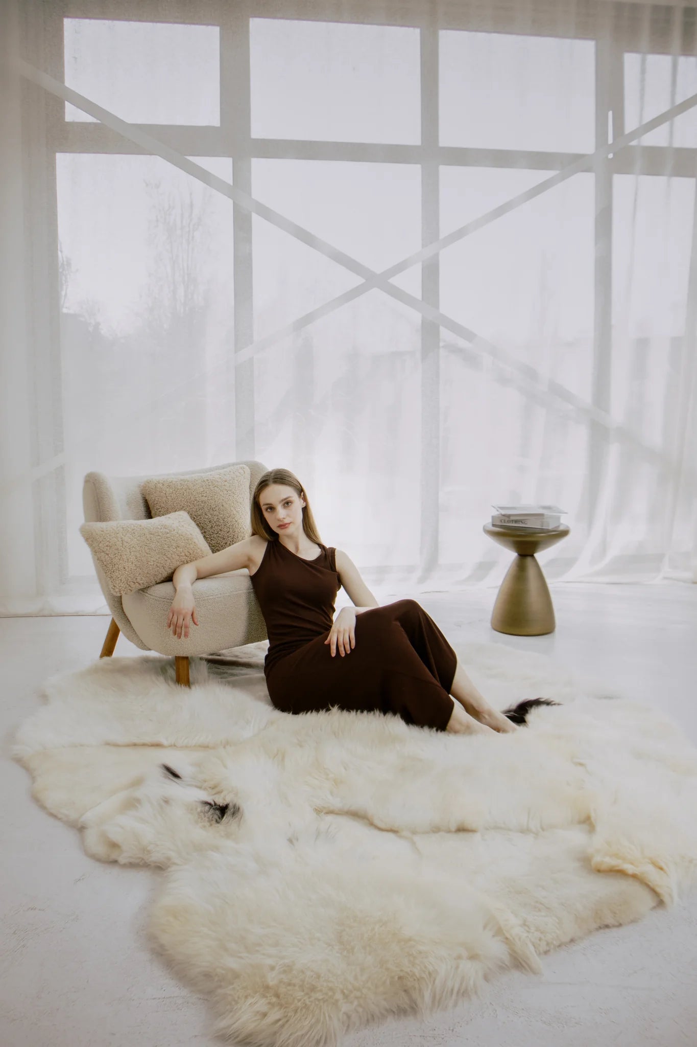 Woman sitting on mixed textured sheepskin rug in a modern room with large windows