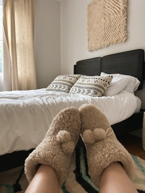 Person wearing organic sheepskin slippers in a bedroom 