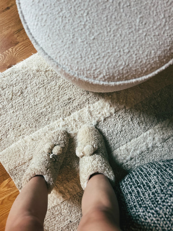Person wearing organic sheepskin slippers a textured rug 
