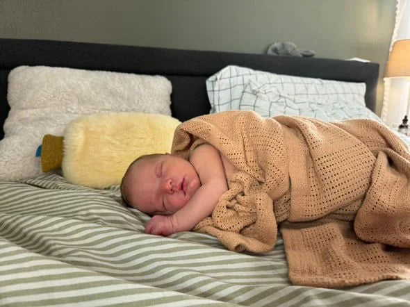 Newborn baby sleeping on a bed with sheepskin hot water bottle warmer