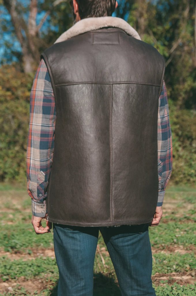 Person wearing a brown sheepskin mens vest outdoors.