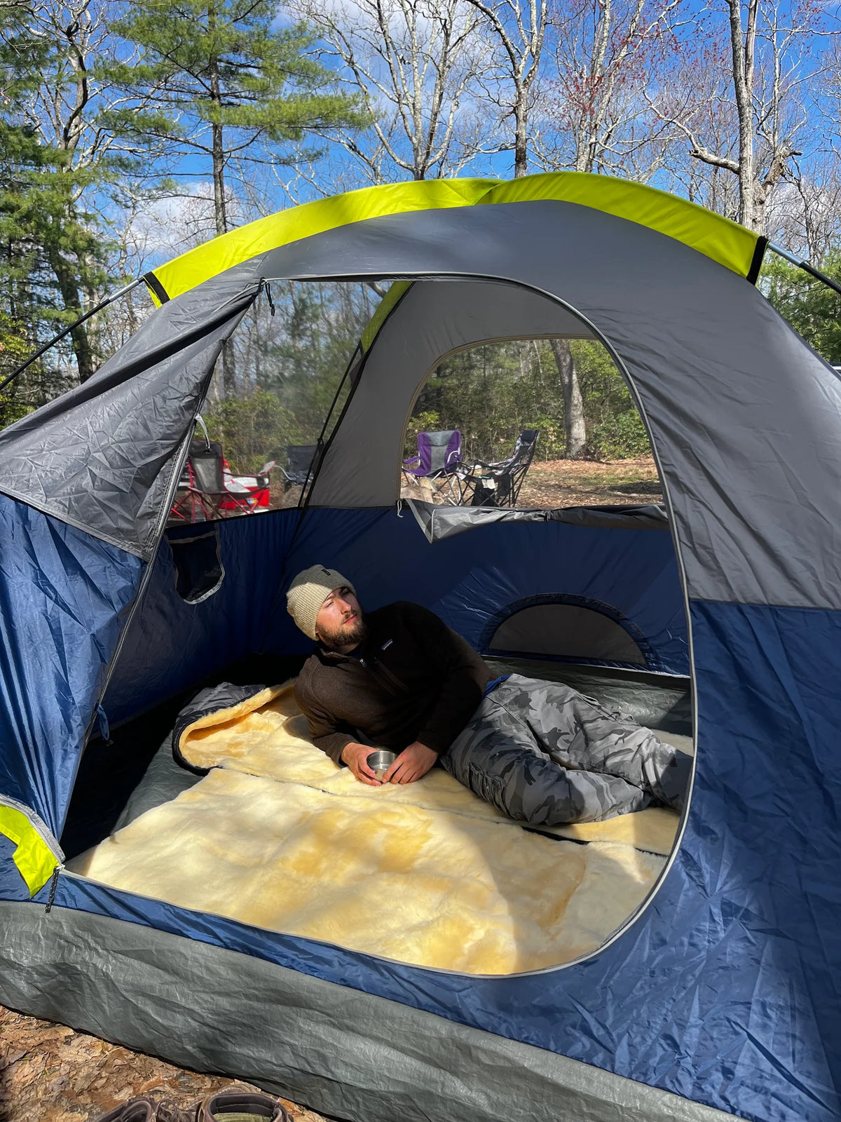 Person lying inside a blue and gray tent on a sheepskin sleeping bag