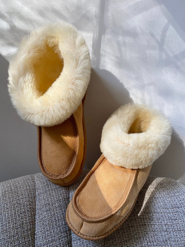 Pair of tan sheepskin slippers placed side by side on a light surface