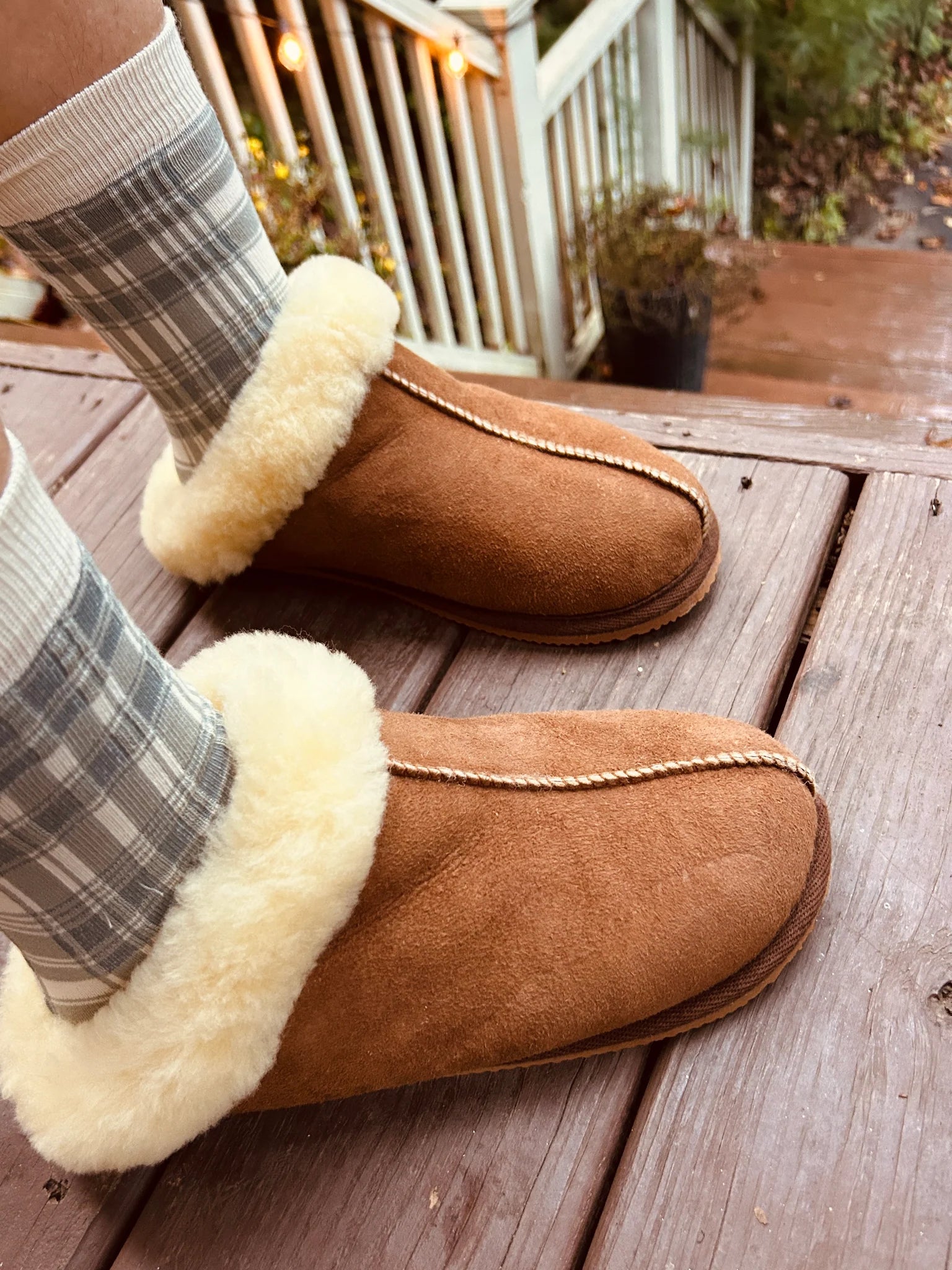 The cottage slipper with white fur lining worn on a wooden deck.