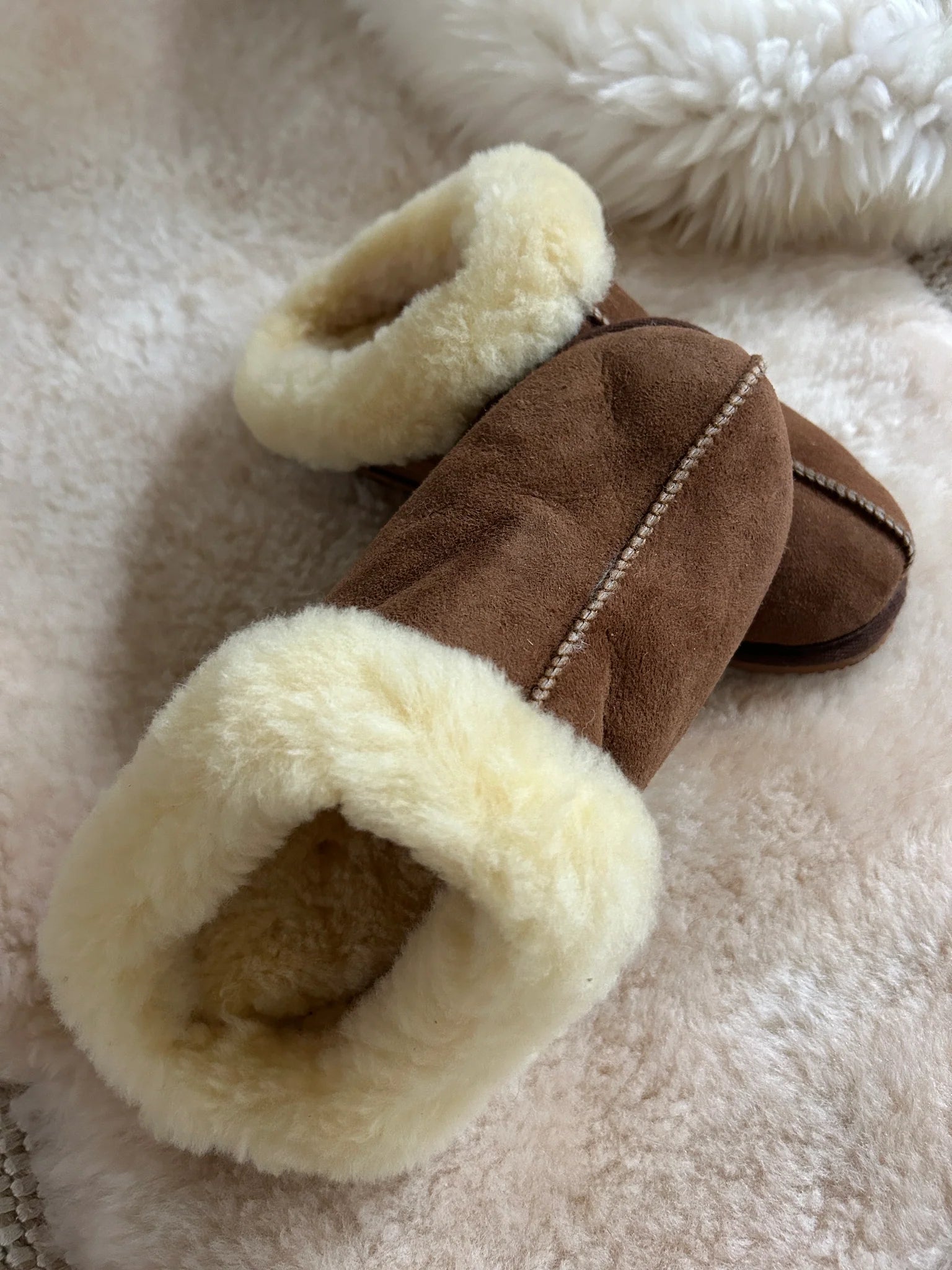 The cottage slipper with white fur lining on a soft beige surface