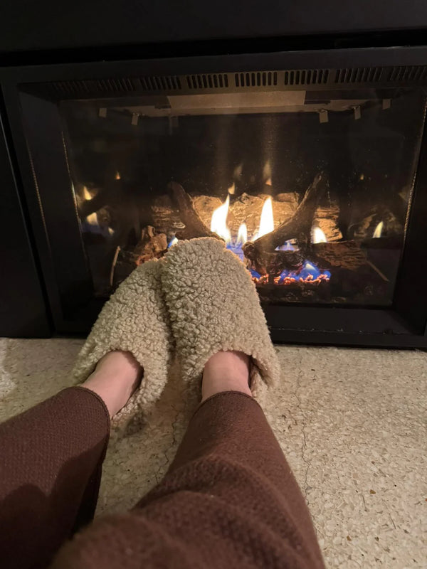 The everyday slip on tan shearling sheepskin by a fireplace with flames visible